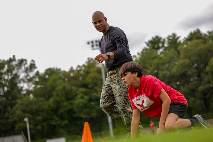 U.S. Marine Corps Capt. Edgardo Diaz, the executive officer of Recruiting Station Boston, directs a Hudson High School football player during the Marine Corps combat fitness test as part of Marine Week Boston, Aug. 21, 2025. During Marine Week Boston, Marines with Marine Corps Recruiting Command shared Marine Corps traditions with local high schools in honor of the Corps’ 250th birthday. Marines stationed across the globe commemorate the 250th anniversary of the Marine Corps, honoring a distinguished legacy of service, sacrifice, and unwavering fidelity to both the nation and fellow Marines. (U.S. Marine Corps photo by Sgt. Aidan Hekker)