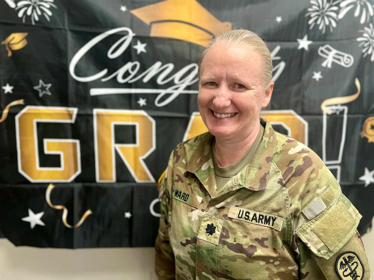 Female Soldier in Uniform standing in front of a graduation banner.