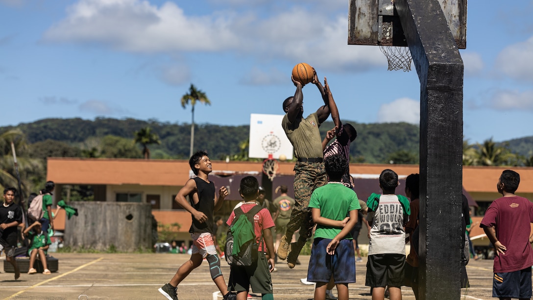 U.S. Marine Corps Staff Sgt. Joshua Mollie, a Georgia native and network chief with Combat Logistics Battalion 15, Combat Logistics Regiment 17, 1st Marine Logistics Group, and local Pohnpeian children play basketball as part of a sports camp during Koa Moana 25 on Pohnpei, Federated States of Micronesia, Aug. 21, 2025.