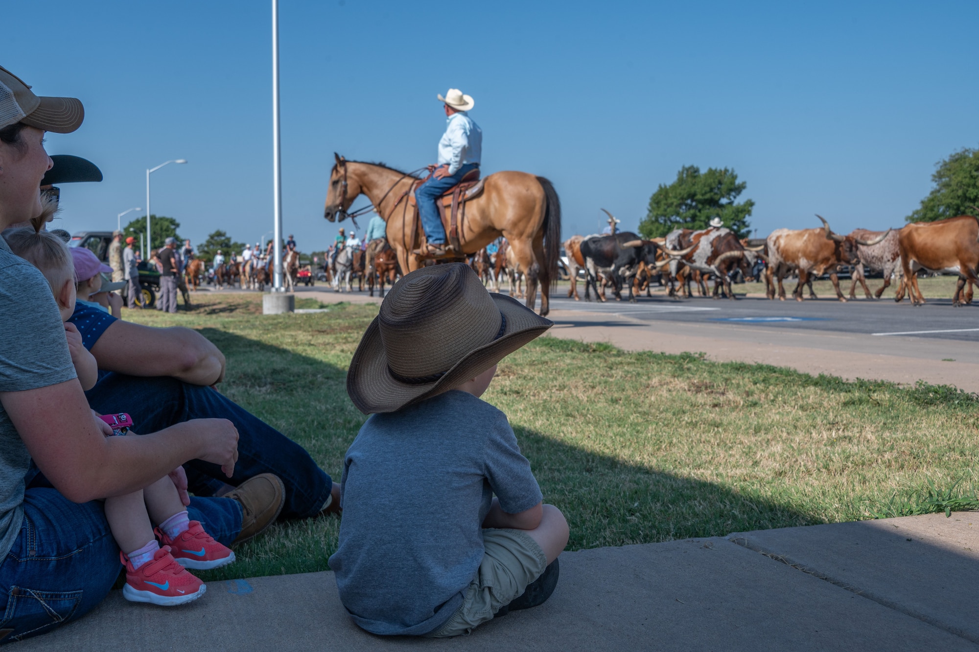 A family watches as the 27th Annual Cattle Drive strolls by at Altus Air Force Base, Oklahoma, Aug. 21, 2025. Airmen and their families lined the streets to catch a glimpse of the rich history and traditions of Altus. (U.S. Air Force photo by Tech. Sgt. Hailey Haux)