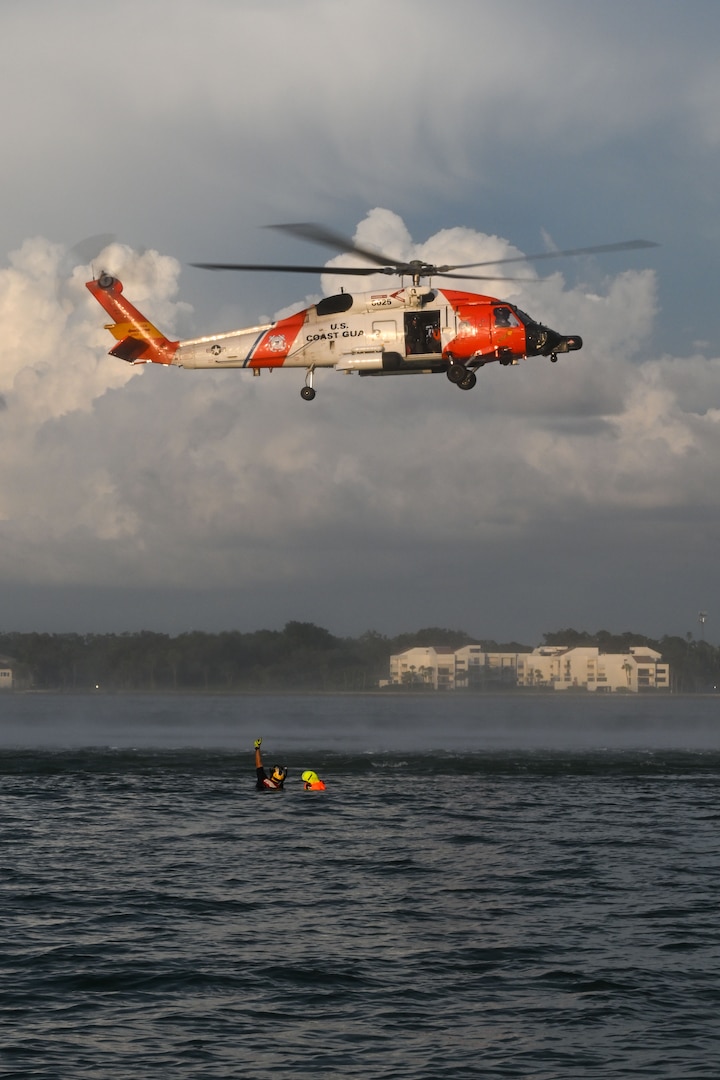 Petty Officer 2nd Class Zachary Loesch, a rescue swimmer assigned to U.S. Coast Guard Air Station Clearwater, signals to the flight mechanic aboard a hovering MH-60 Jayhawk during search and rescue training in Sand Key, Florida, Aug. 13, 2025. U.S. Coast Guard flight mechanics are responsible for conducting hoist operations and directly control how the swimmer is raised or lowered by the hoist cable. (U.S. Coast Guard photo by Petty Officer 1st Class Riley Perkofski)