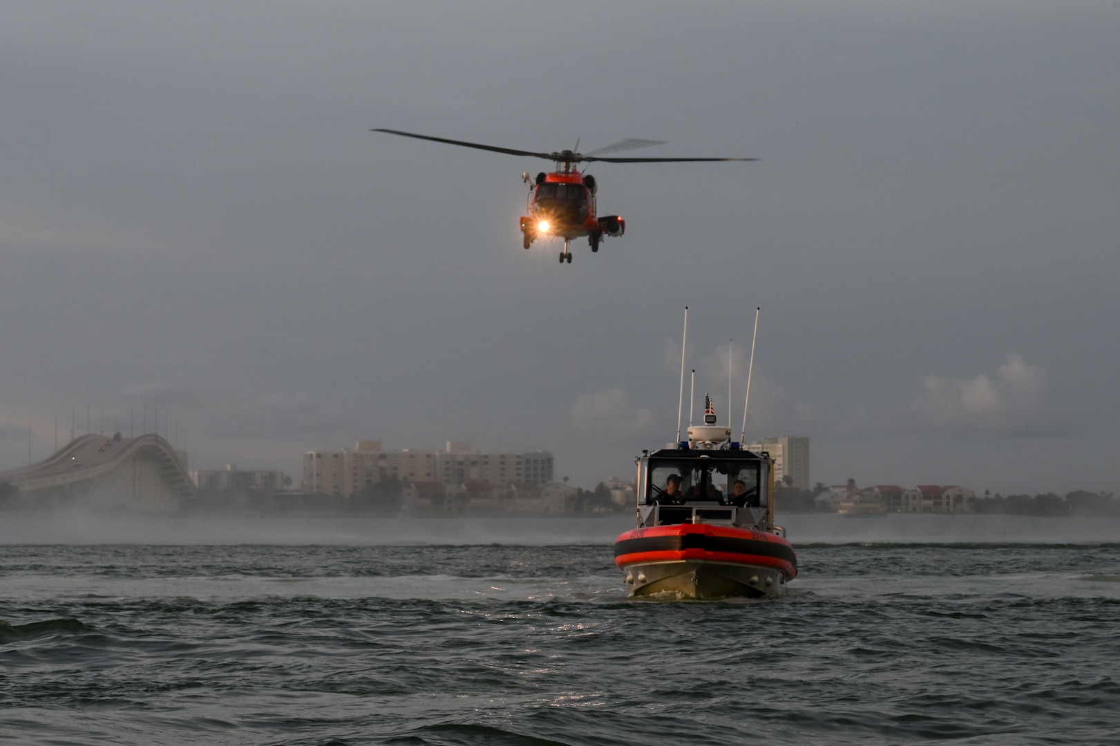 A U.S. Coast Guard Air Station Clearwater MH-60 Jayhawk aircrew flies behind a U.S. Coast Guard Station Sand Key 29-foot response boat-small boat crew during training in Sand Key, Florida, Aug. 13, 2025. U.S. Coast Guard Sector St. Petersburg boatcrews regularly hold hoist training with Air Station Clearwater aircrews to maintain their qualifications and crew readiness. (U.S. Coast Guard photo by Petty Officer 1st Class Riley Perkofski)