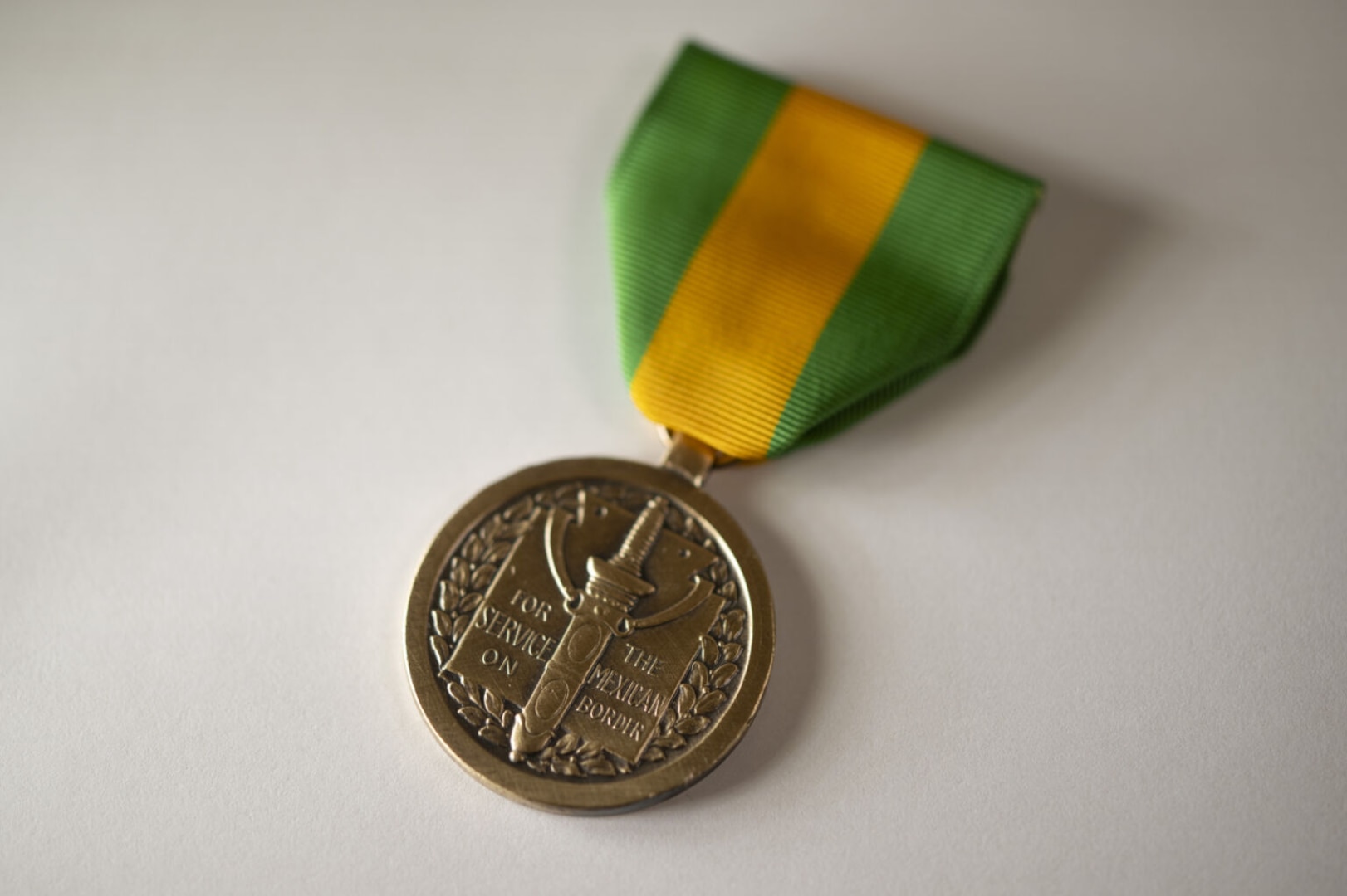 A bronze round military medal hangs from a yellow and green striped ribbon with a clasp.