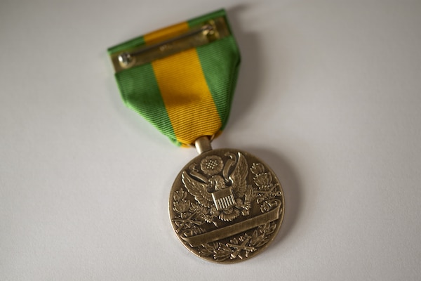 A bronze round military medal hangs from a yellow and green striped ribbon.