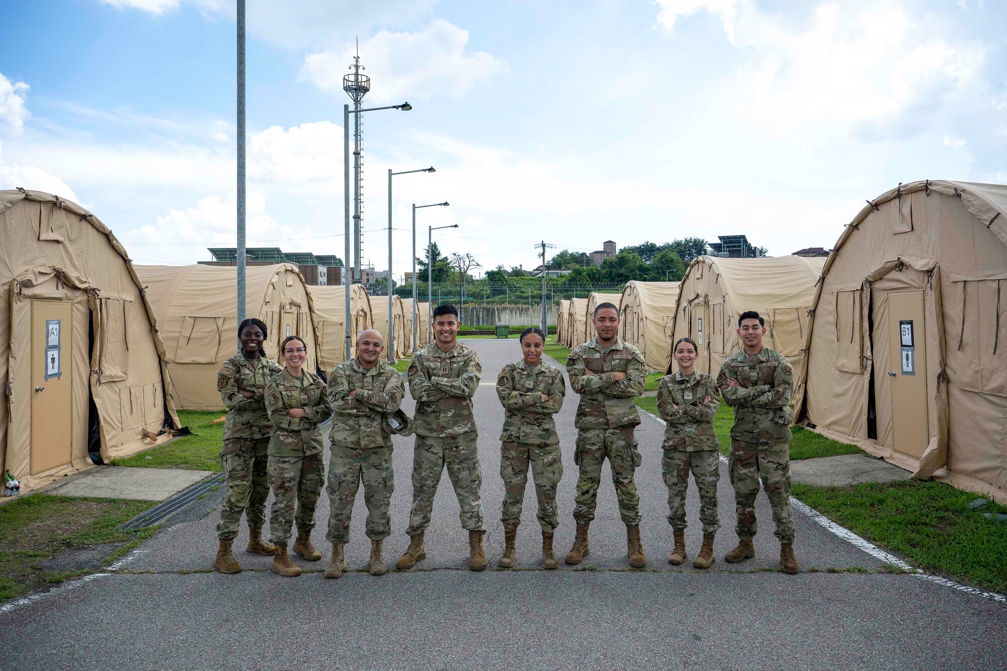 A group of people pose for a group photo outside of rows of tents on a paved road.