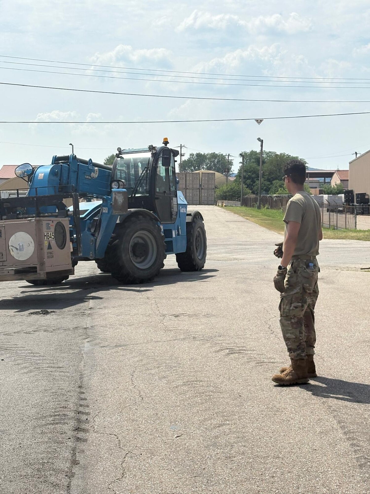 A man stands outside watching an A/C unit being hauled by heavy machinery