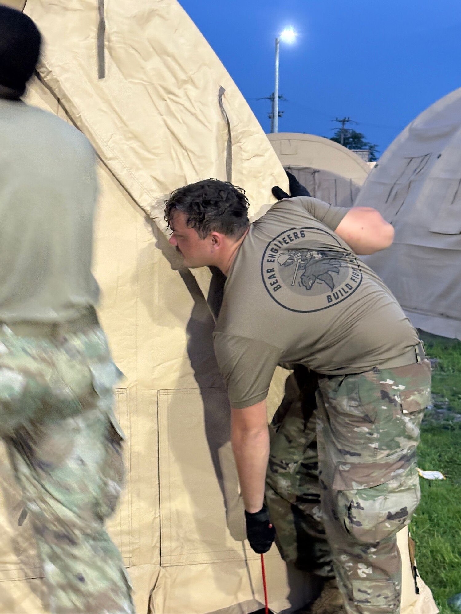 A person is pulling on a rope of a large tent in bare-base conditions.