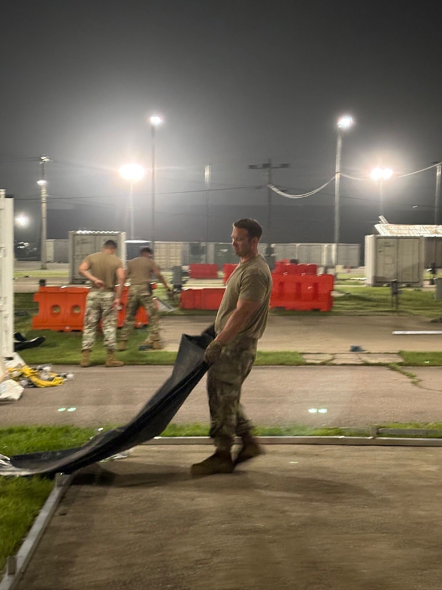 A person drags a tarp along the ground at night in bare-base conditions.