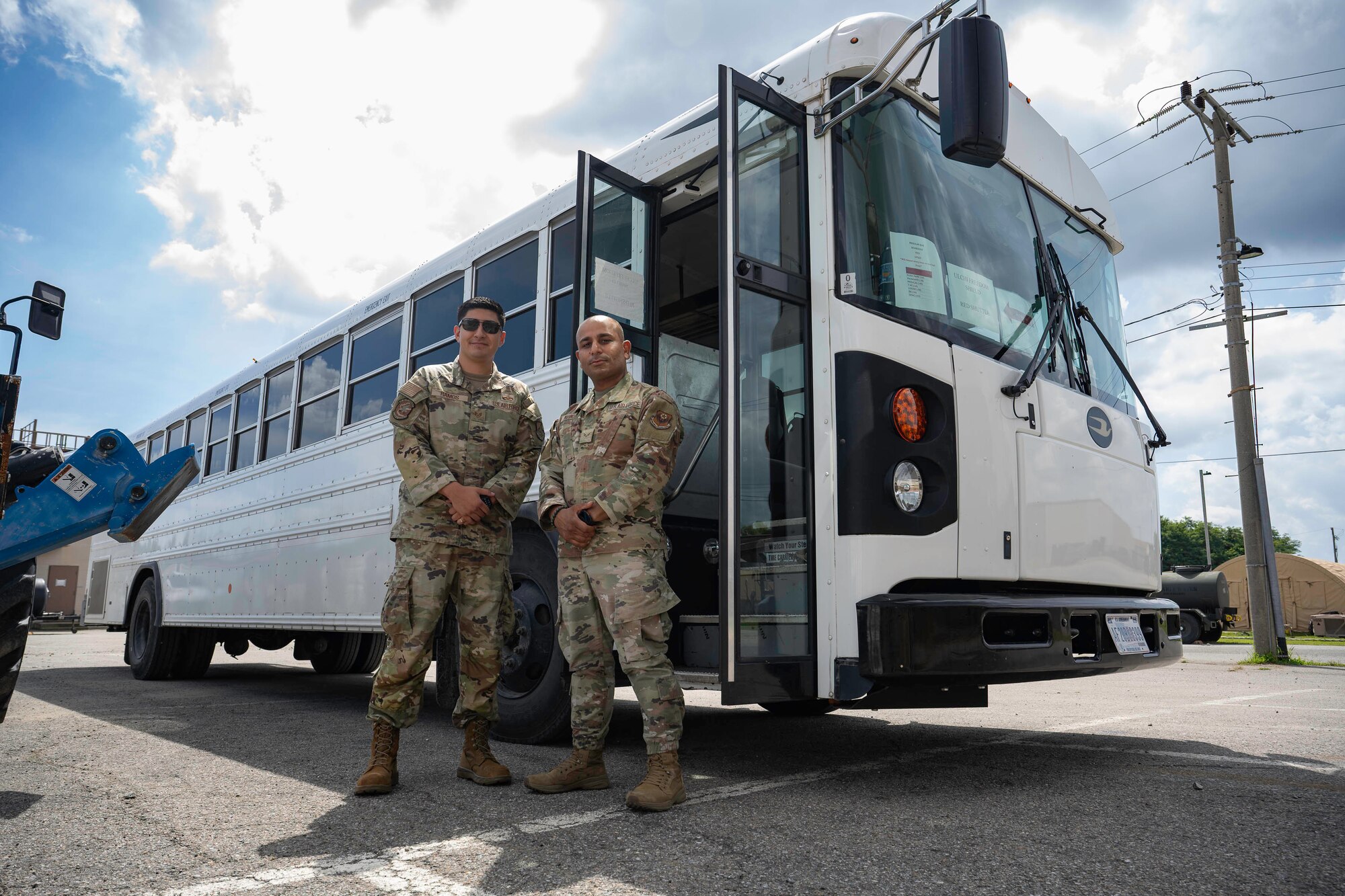 Two people stand in front of a white bus.
