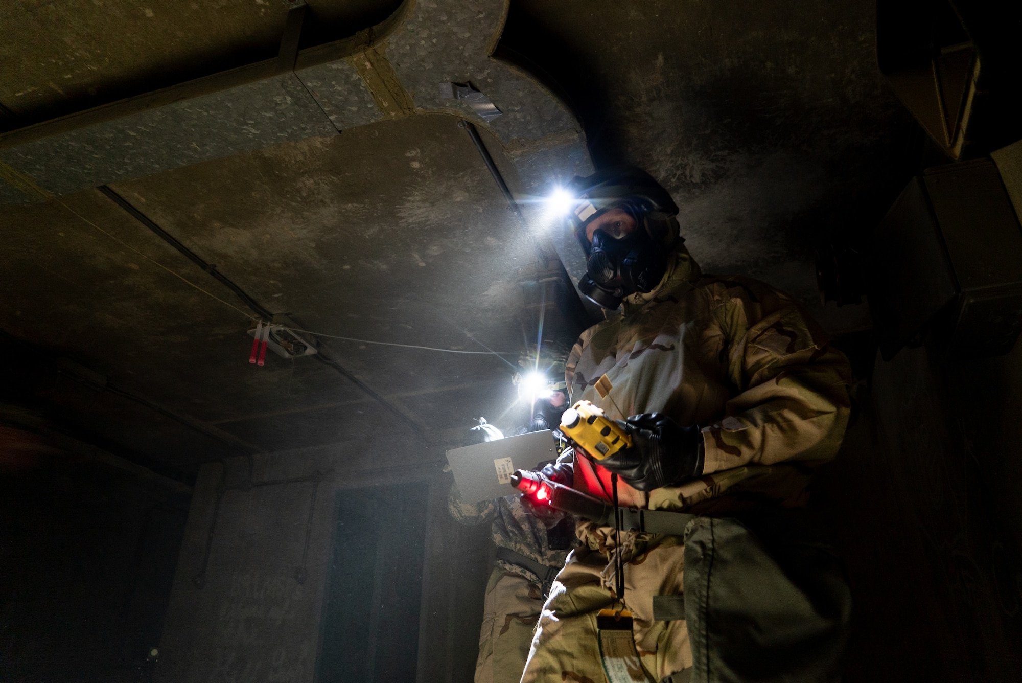 A 386th ECES on the righthand side holds chemical detection devices as his headlamp illuminates the bunker