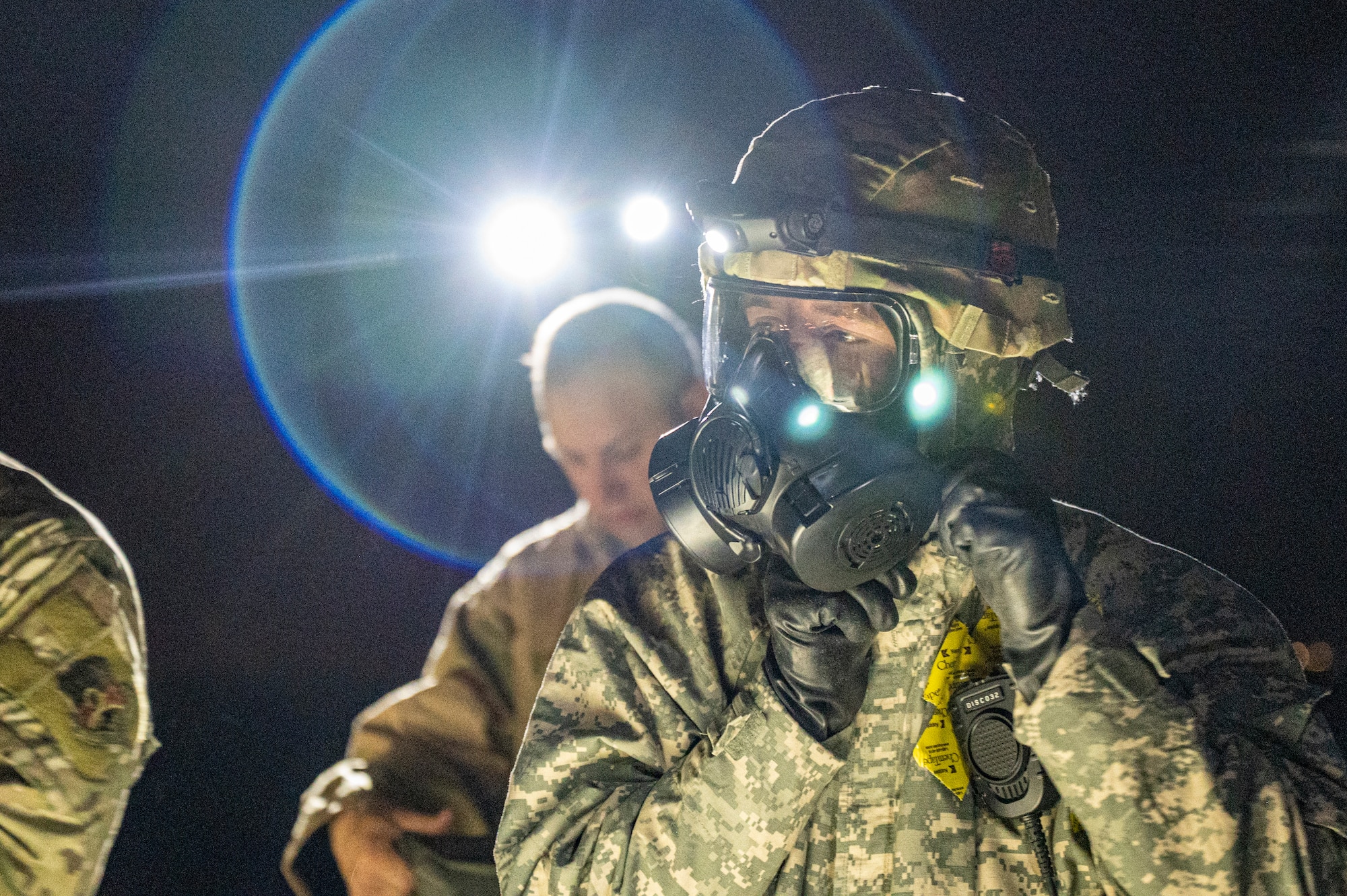 A 386th ECES Airman dons his gas mask in the foreground