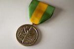 A bronze round military medal hangs from a yellow and green striped ribbon with a clasp.