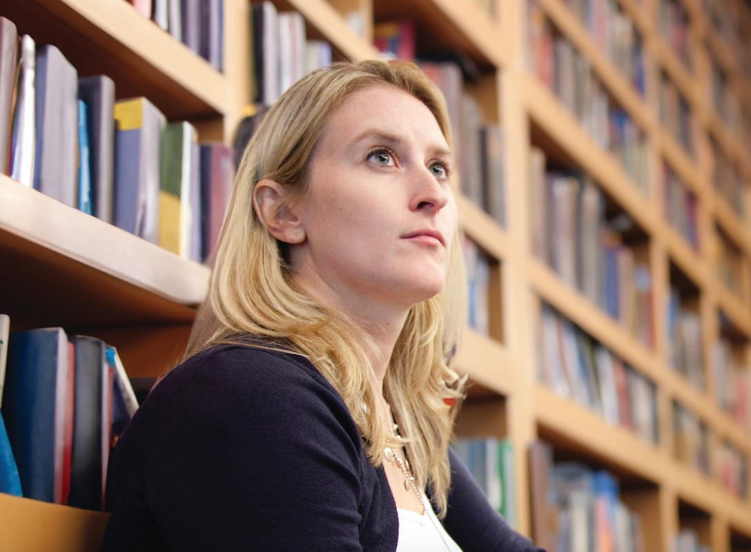 Internet Publications Editor Joey Seich looks up as she sits in front of a bookcase in the library at National Defense University in Washington, D.C.
