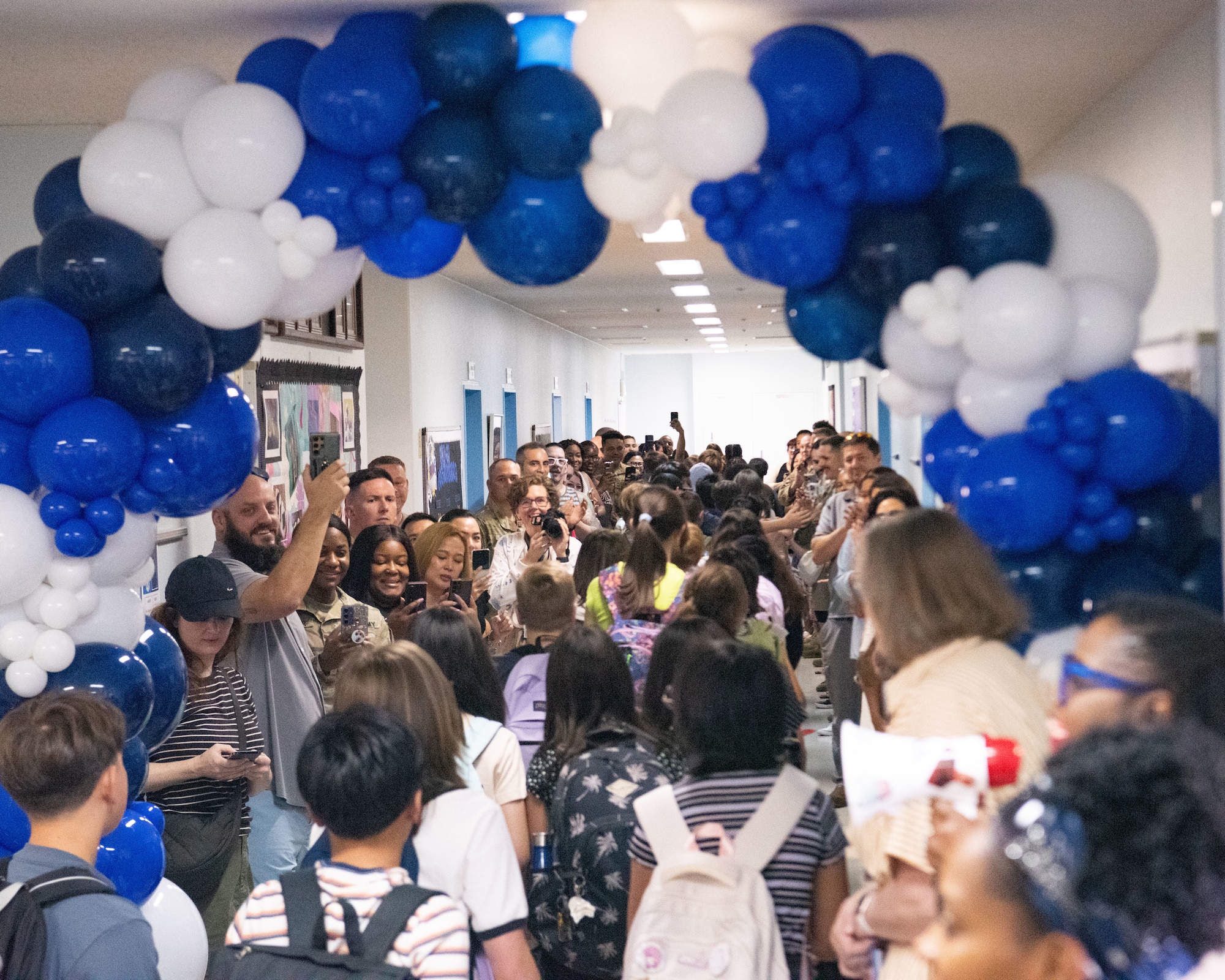Schoolchildren walk through a hallway lined with balloons and parents.