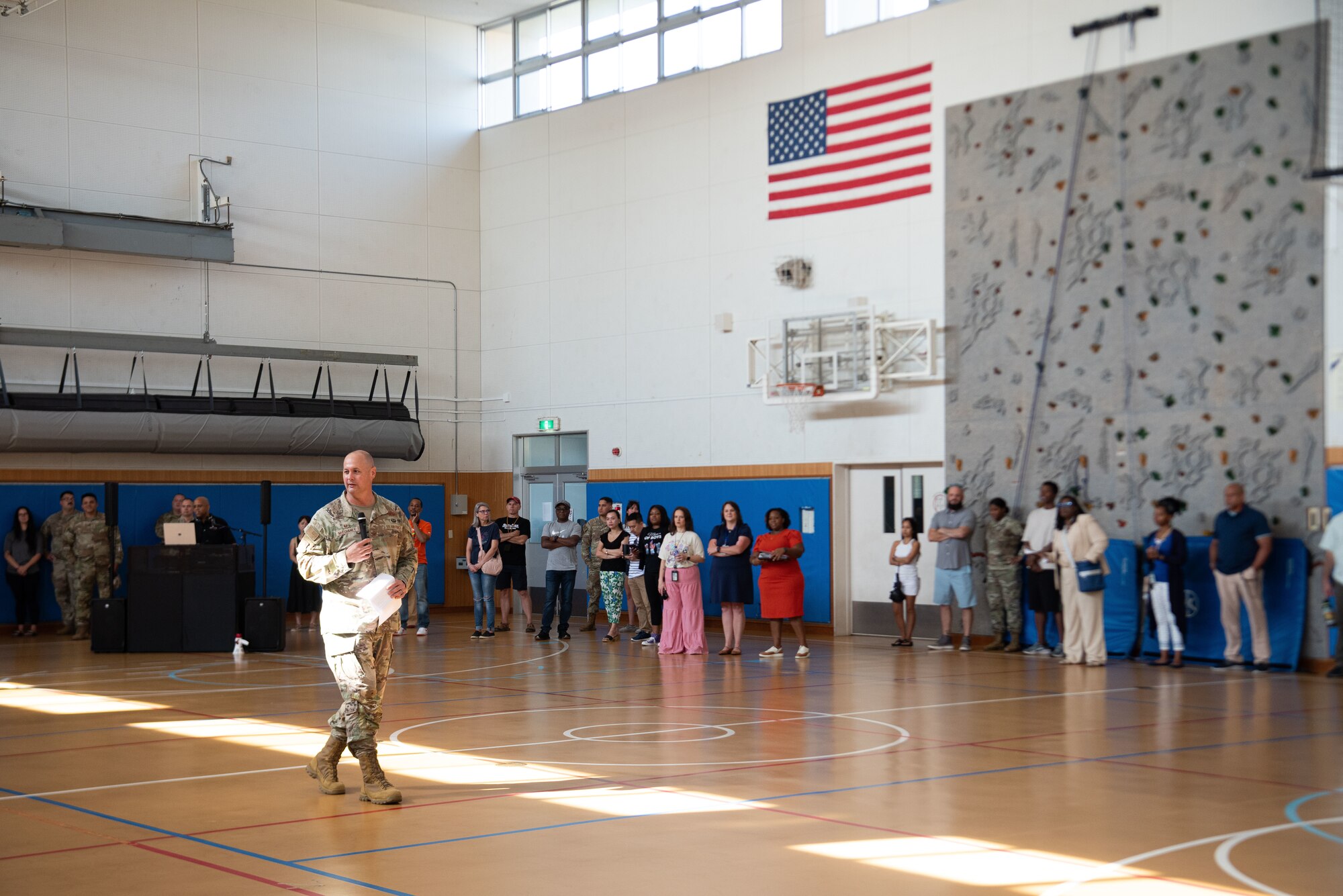 A U.S. servicemember speaks to people in a school gymnasium.