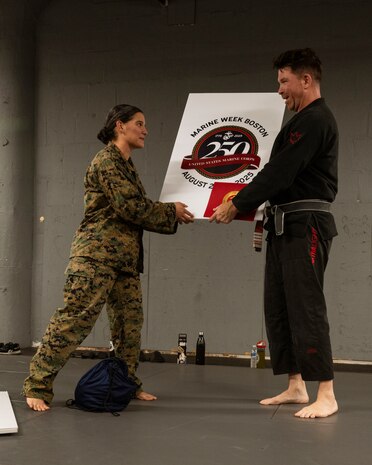 U.S. Marine Corps 1st Lt. Hope Nelson, a planning officer assigned to Special Purpose Marine Air-Ground Task Force-250, gives a gift to John Clarke, owner of Broadway Jiu-Jitsu, after a martial arts collaboration at Broadway Jiu-Jitsu during Marine Week Boston, Aug. 22, 2025. Marines stationed across the globe commemorate the 250th anniversary of the Marine Corps, honoring a distinguished legacy of service, sacrifice, and unwavering fidelity to both the nation and fellow Marines. (U.S. Marine Corps photo by Cpl. Vincent Needham)