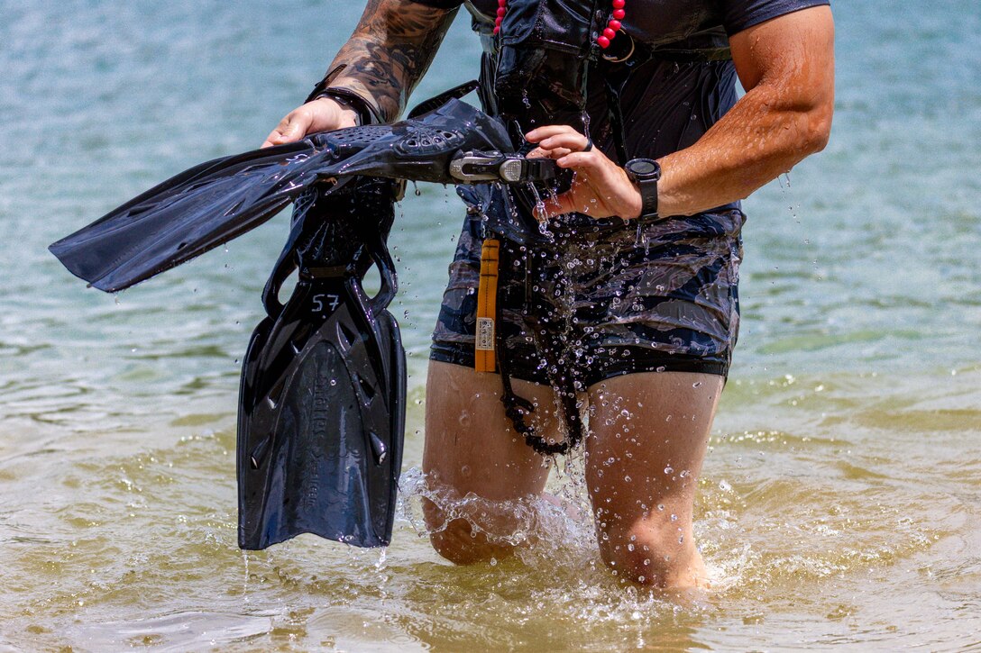 A man holding diving equipment emerges from a lake.