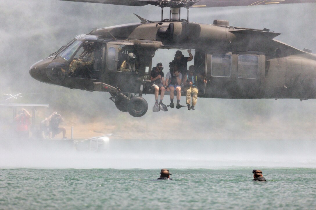 Men jump out of a military helicopter into a lake.