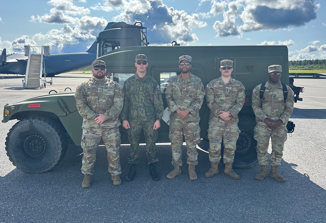 Virginia National Guard Soldiers and a Finnish soldier stand in front of a Humvee