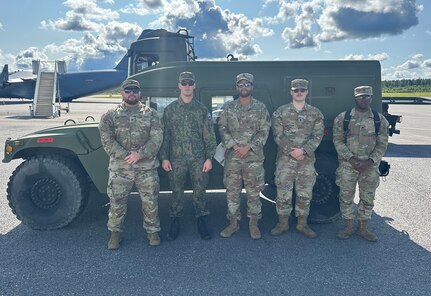 Virginia National Guard Soldiers and a Finnish soldier stand in front of a Humvee