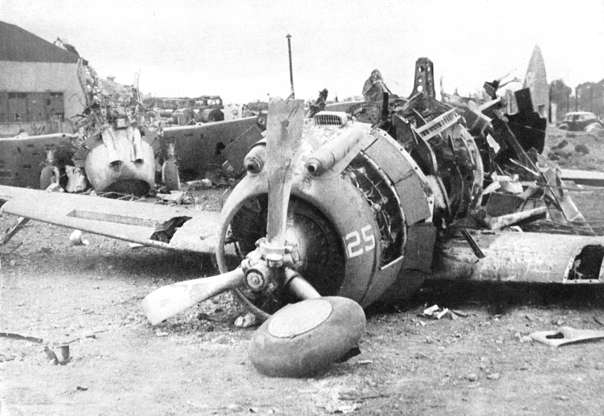 Destroyed P-35 aircraft sitting on the runway in front of a hangar; it's wings and fuselage badly damaged