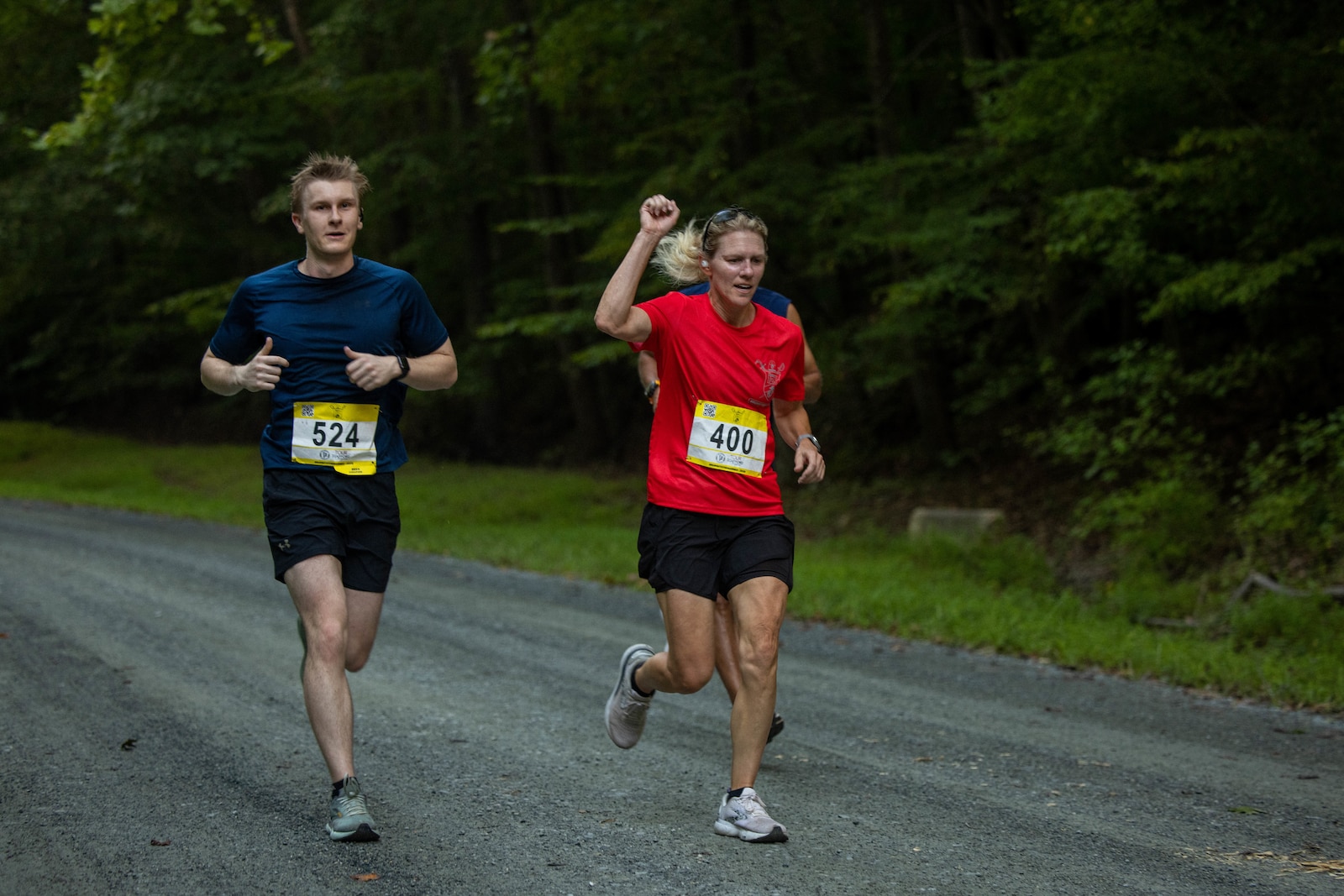 U.S. Marine Corps Col. Jenny Colgate, center, the commanding officer of Marine Corps Base Quantico, encourages runners while participating in the Quantico 12K on MCBQ, Virginia, Aug. 23, 2025. Colgate is a native of Lorton, Virginia. The event challenges runners and their individual tenacity as they ran 7.46 miles of trails through the woods of Marine Corps Base Quantico's Officer Candidate School. (U.S. Marine Corps photo by Lance Cpl. Federico Marquez)