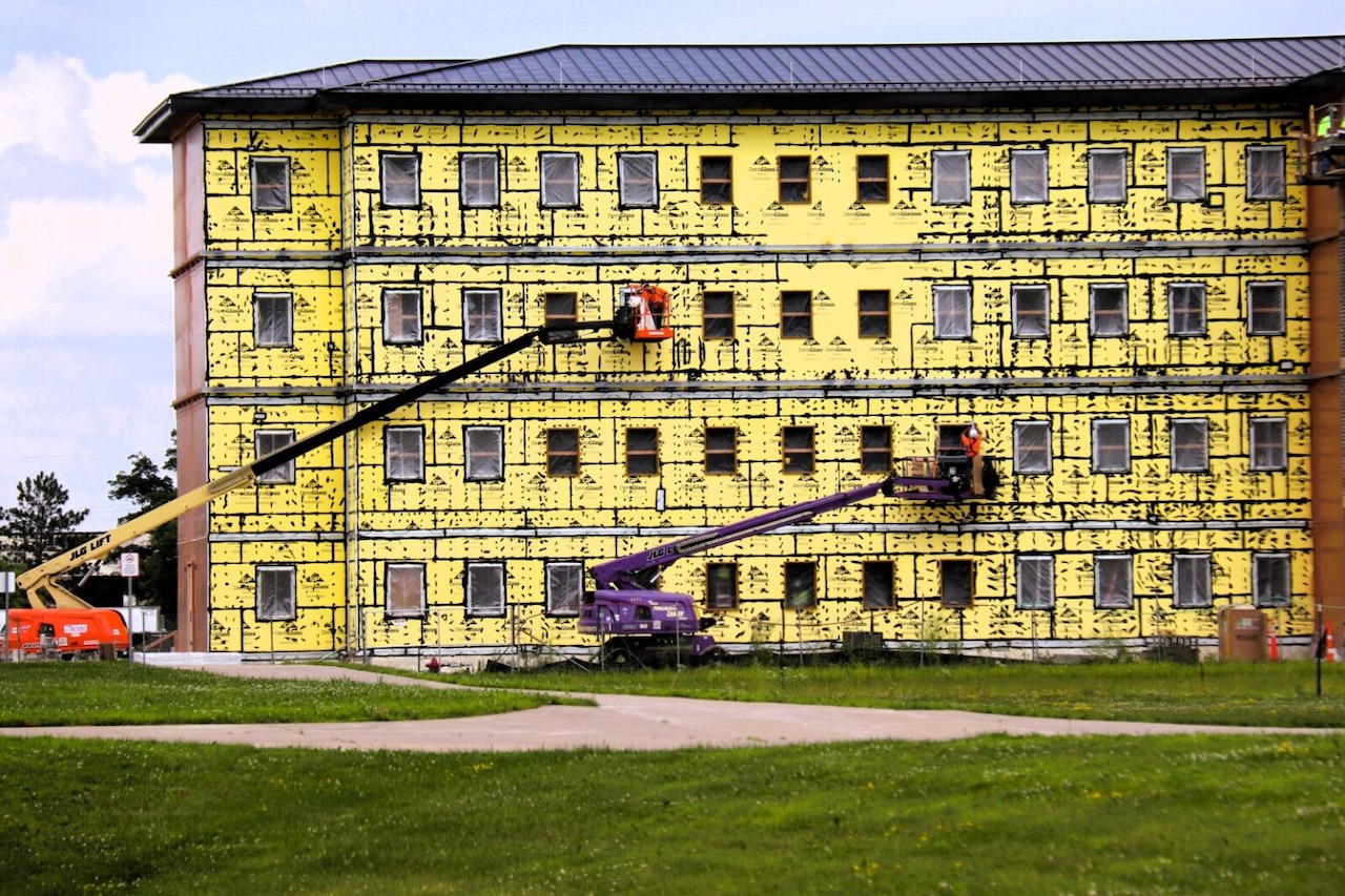 Two construction workers use lifts to reach the second and third floors of a building that is under construction.