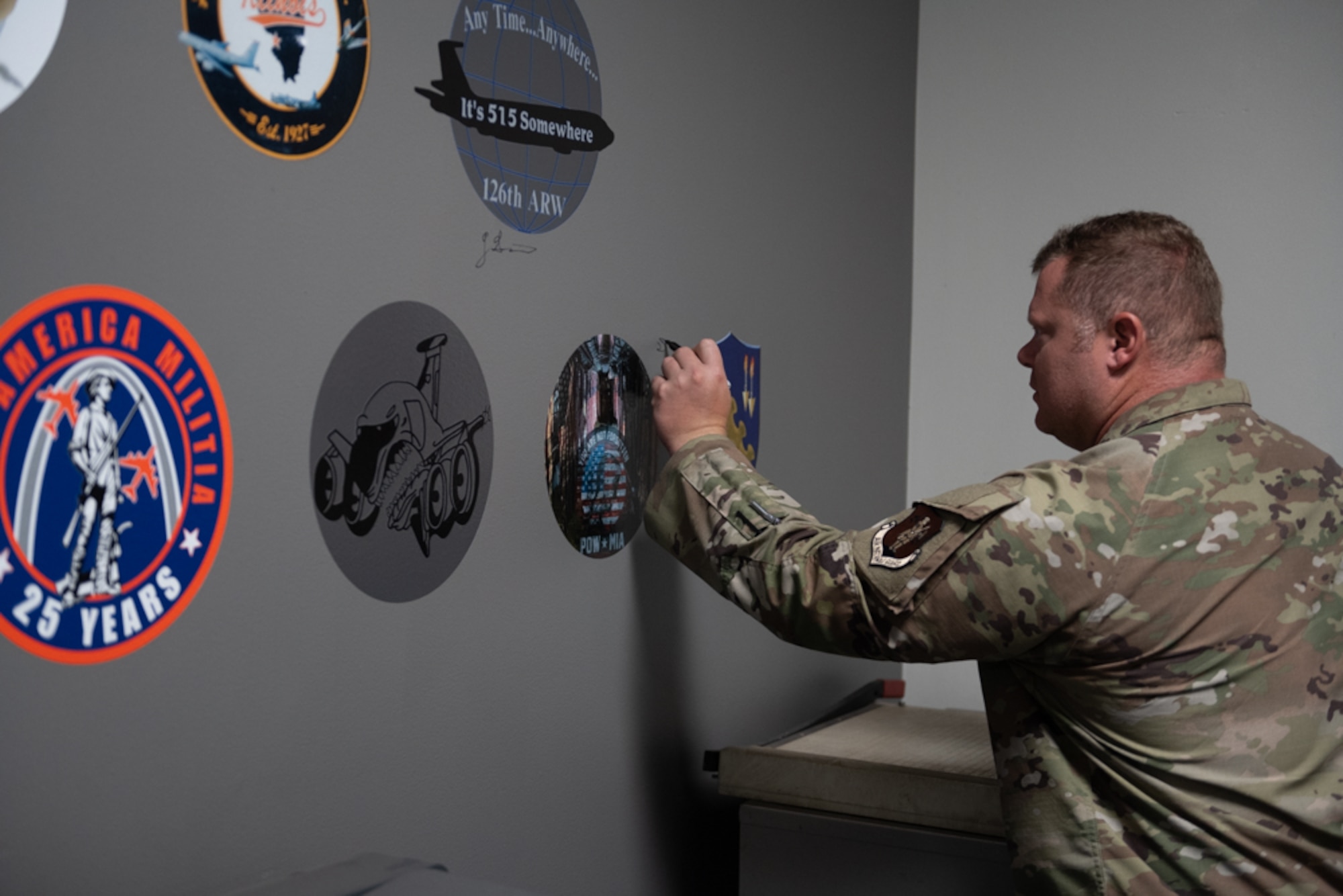 a male airman signing his name to a gray wall surrounded by aircraft nose art.