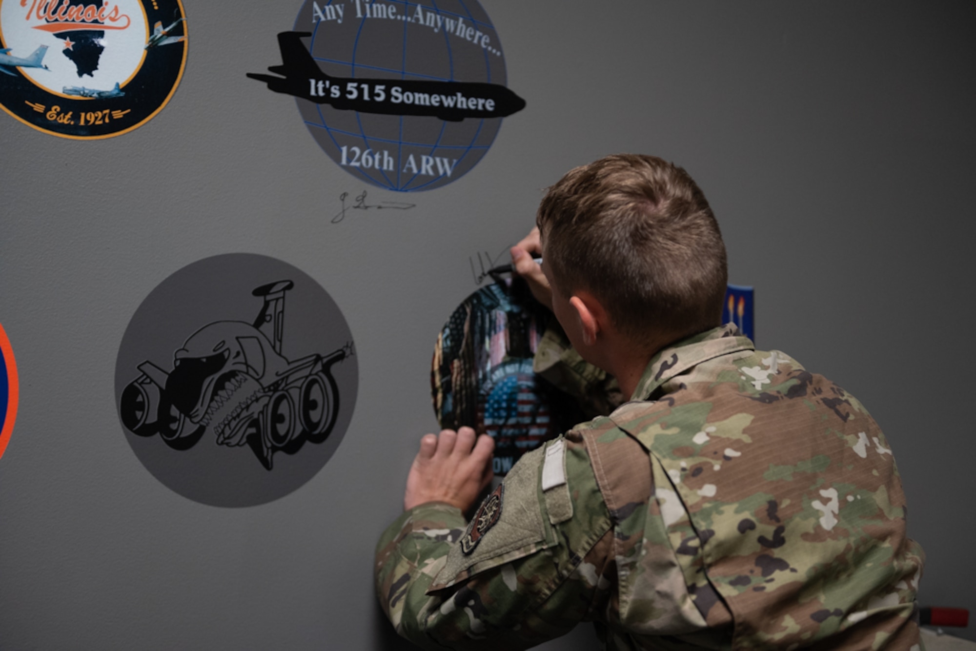 a male airman signing his name to a gray wall around the nose art he is assigned to.