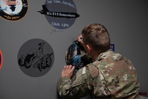a male airman signing his name to a gray wall around the nose art he is assigned to.