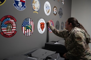 A woman airman with a ponytail signing her name on a gray wall with nose art.