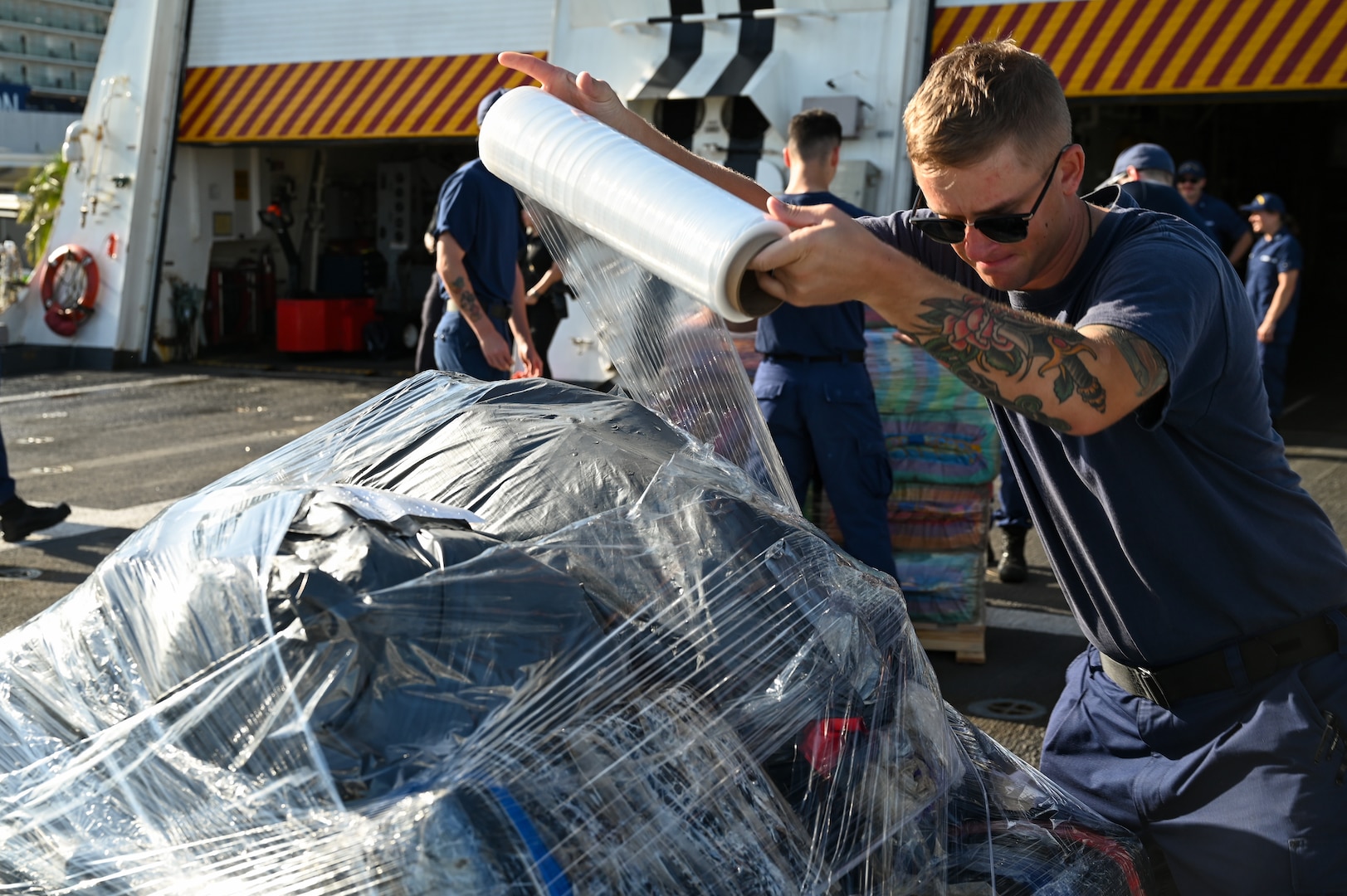 A U.S. Coast Guard Cutter Hamilton (WMSL 753) crew member plastic wrapping drugs during an offload of approximately 76,140 lbs of illicit narcotics at Port Everglades, Florida, on August 25, 2025. This offload was the result of 19 separate interdictions in the Eastern Pacific Ocean and the Caribbean. (U.S. Coast Guard photo by Petty Officer 3rd Class Nicholas Strasburg)