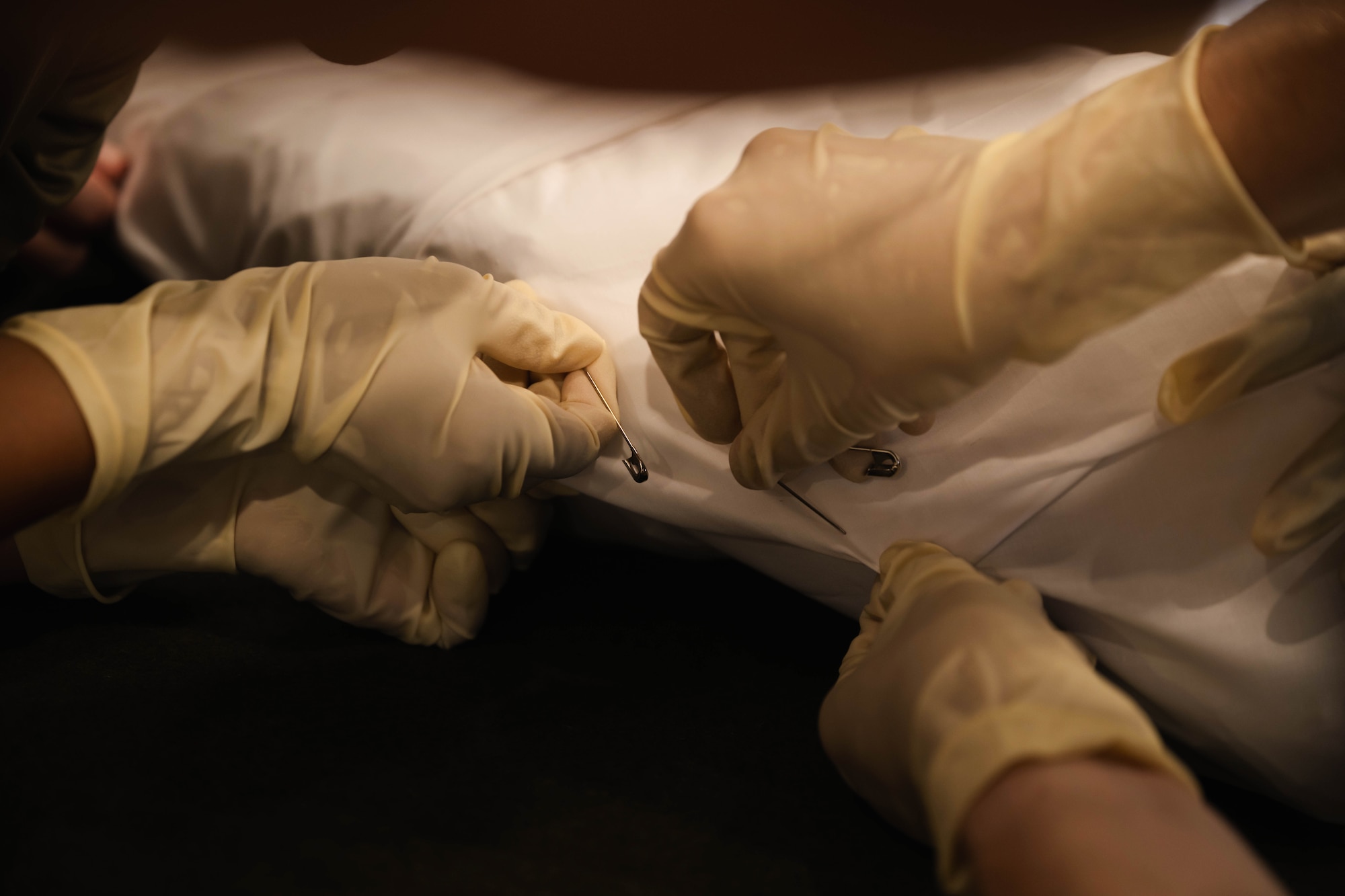 U.S. Marines from the Personnel Retrieval and Processing Company, a part of annual exercise Northern Strike 25-2, pin a white sheet during body wrap training at Grayling Army Airfield, Michigan, Aug. 10, 2025. The body-wrap procedures were taught by Air Force Mortuary Affairs Operations personnel during the exercise of their expeditionary mortuary. (U.S. Air Force photo by Senior Airman Madeline Baisey)