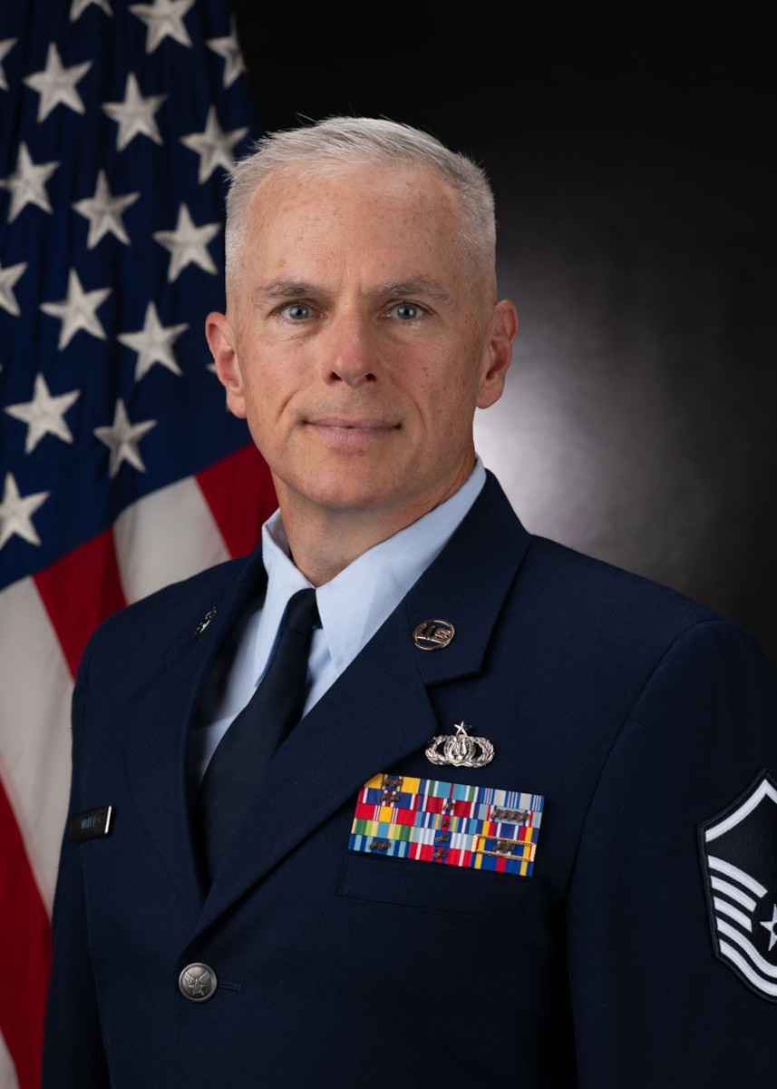 Official Photo of MSgt Joseph Whitt, bass with the USAF Band of the Pacific-Asia.  MSgt Whitt is wearing blue service dress in front of the American flag.