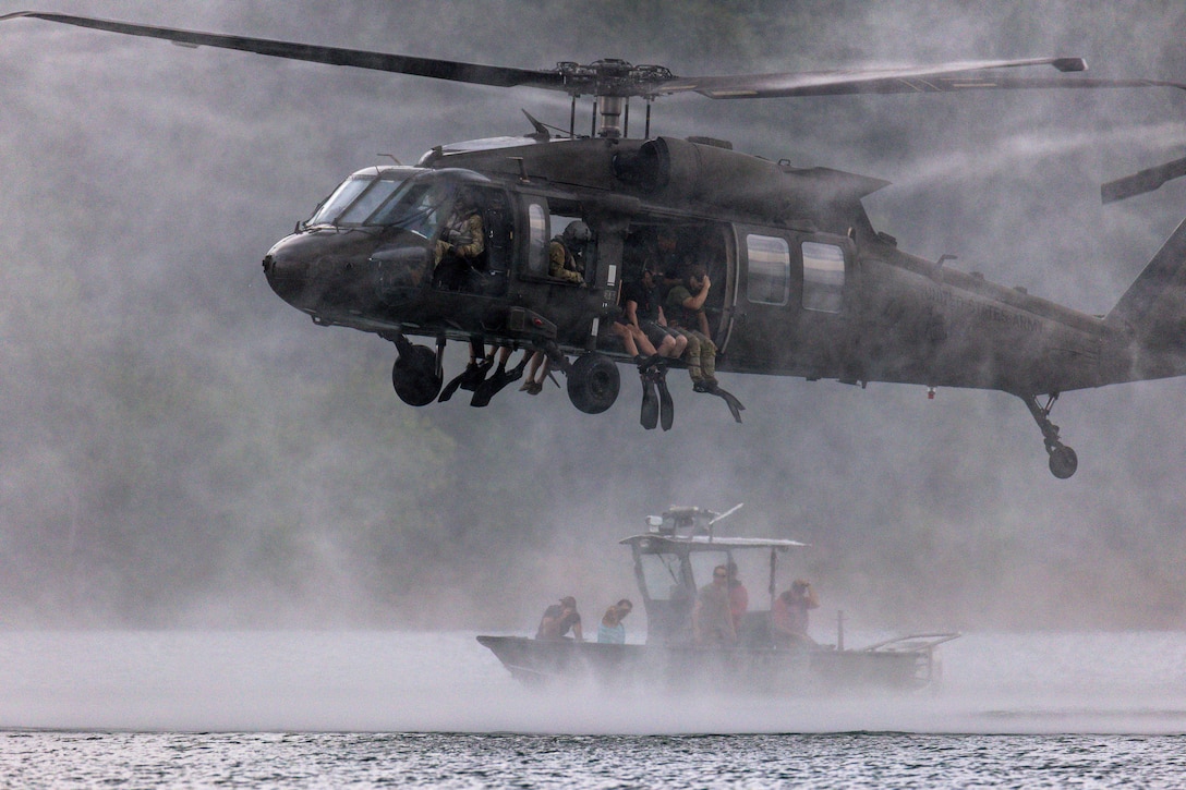 Men jump out of a military helicopter into a lake.