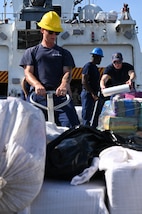 The crew of U.S. Coast Guard Cutter Hamilton (WMSL 753) moving illicit drugs on the flight deck on August 25, 2025, at Port Everglades, Florida. The drugs were transferred to partners such as the Drug Enforcement Agency for processing and destruction. (U.S. Coast Guard photo by Petty Officer 3rd Class Nicholas Strasburg)