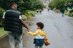 Father and son hold hands while walking down a street