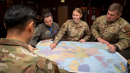 Staff Sgt. Eleanor Warren points to a location on a map while three Airmen observe.