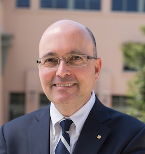 Edl Schamiloglu looks into the camera for his headshot wearing glasses, a suit jacket, white button down shirt, and tie.