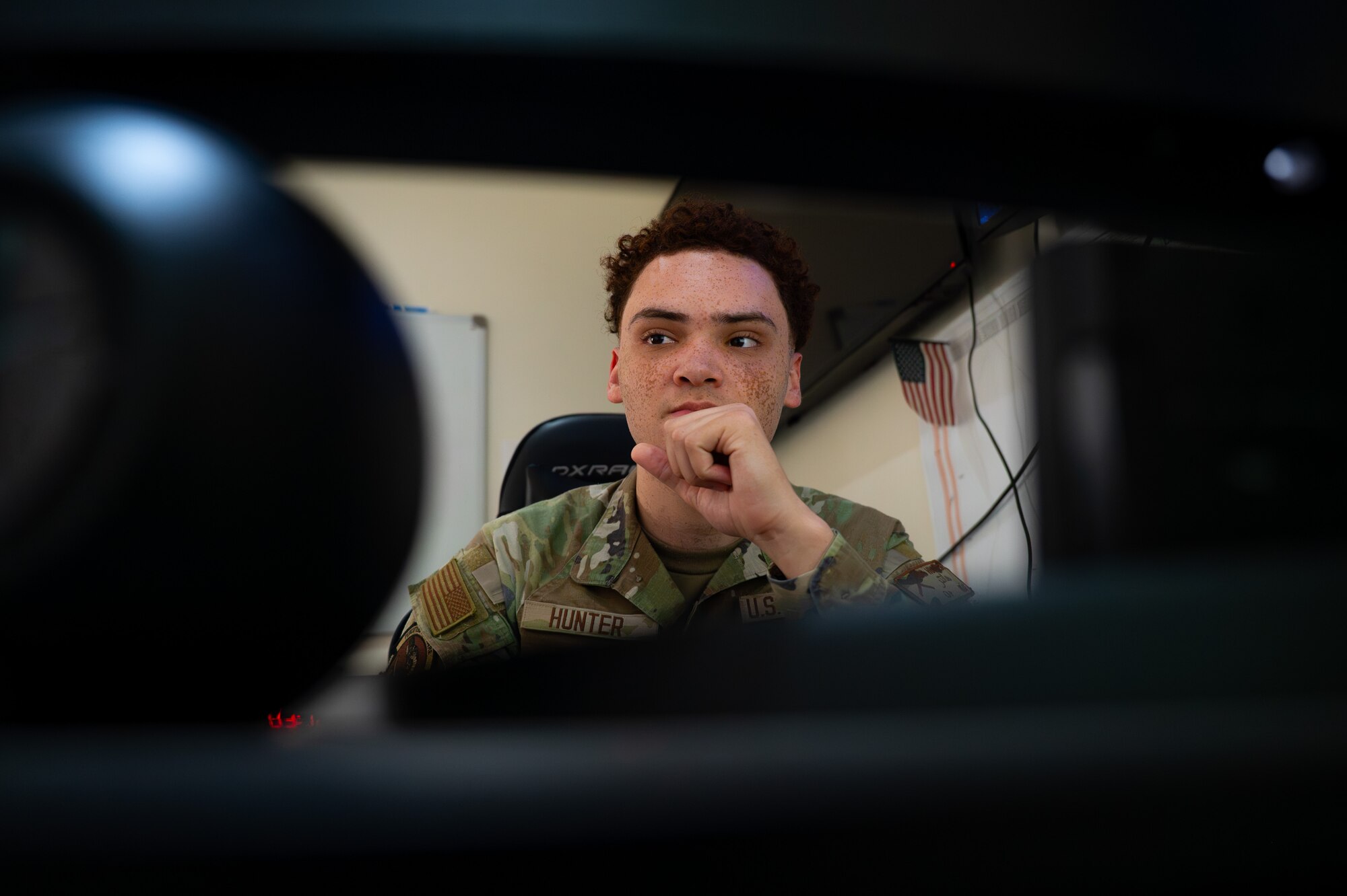 Airman sits behind a desk and looks at a computer screen