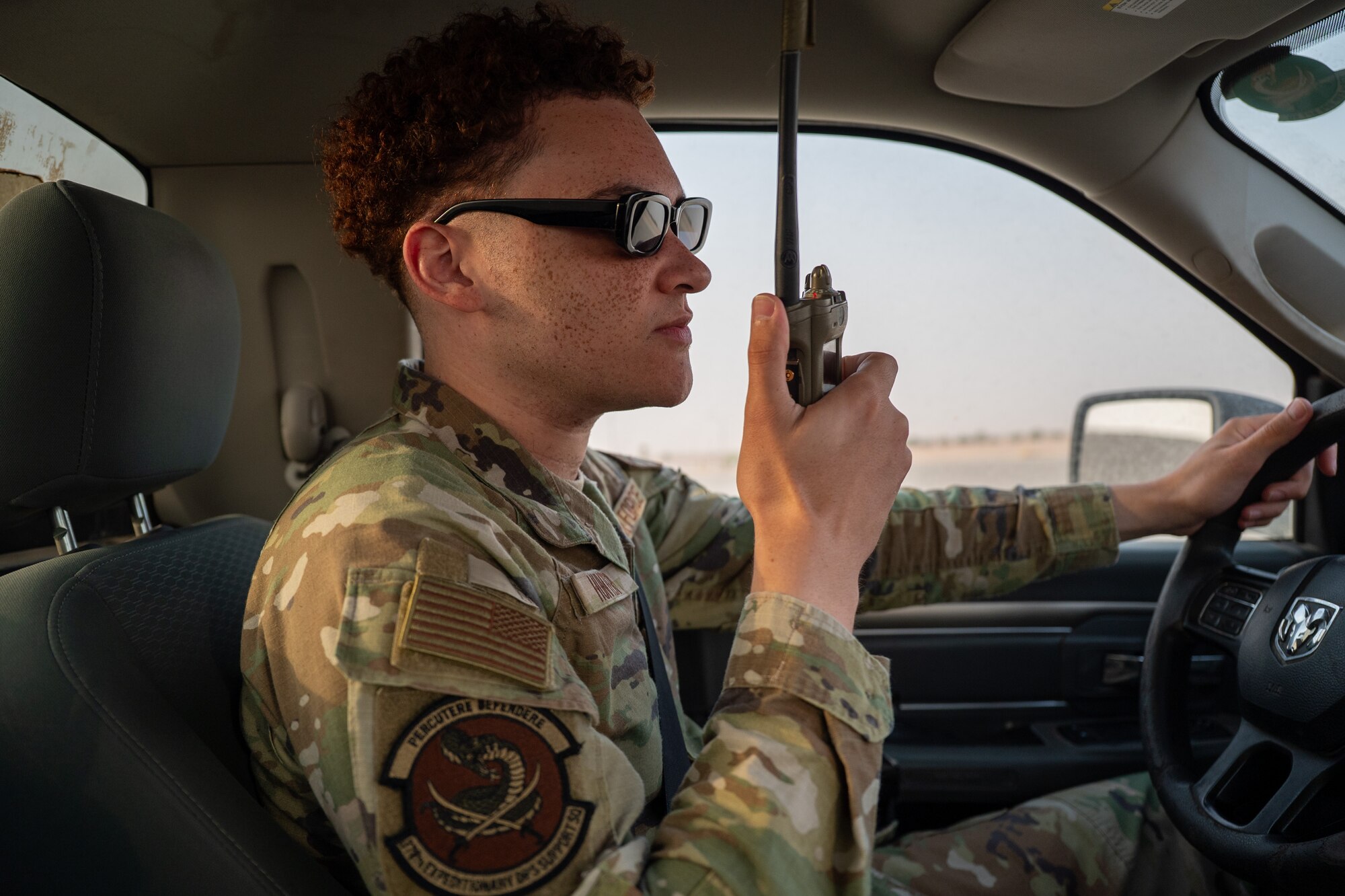 Airman sits in the drivers seat of a truck and holds a land mobile radio