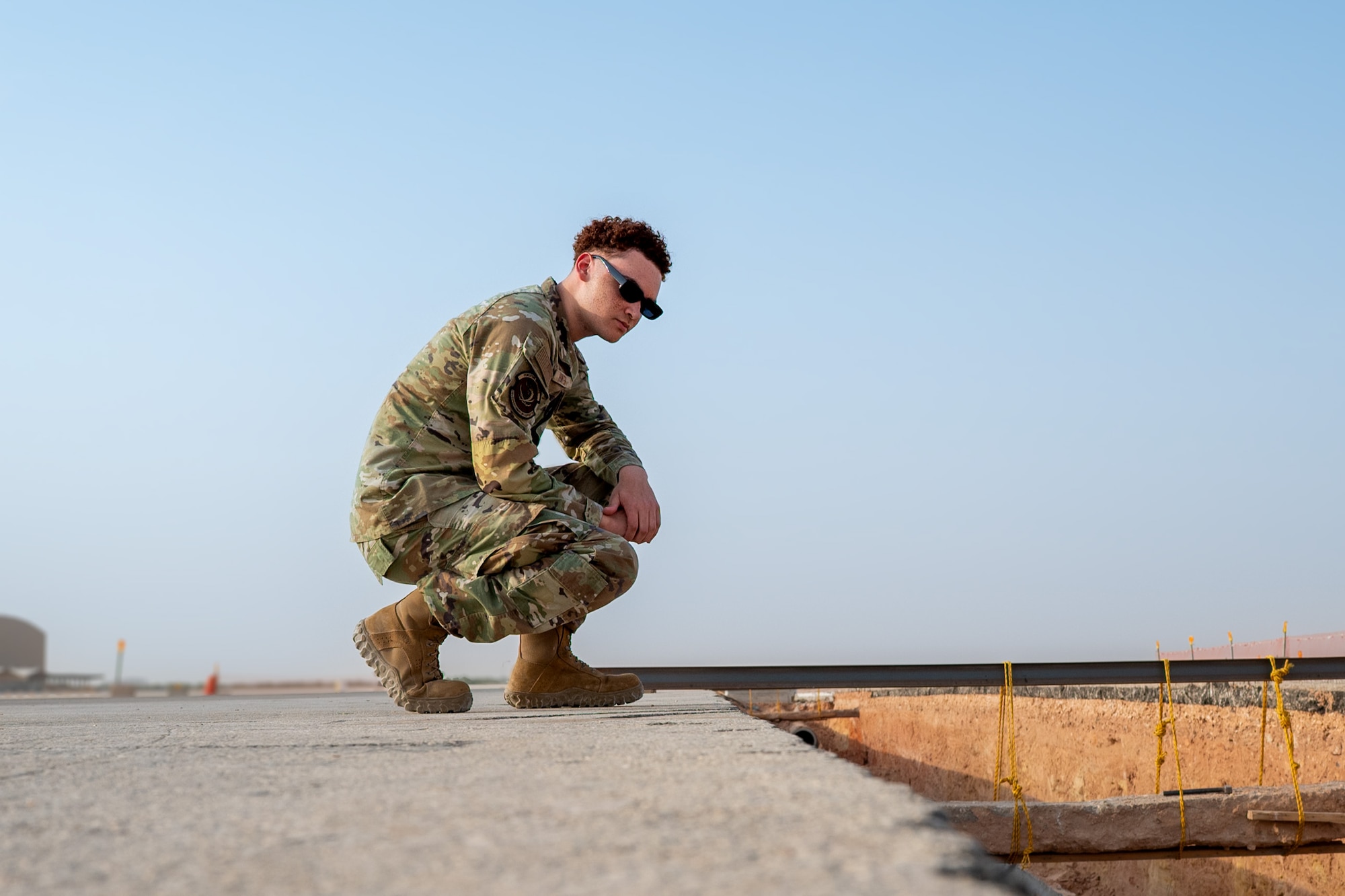 Airman crouches down to inspect a construction site on the flightline