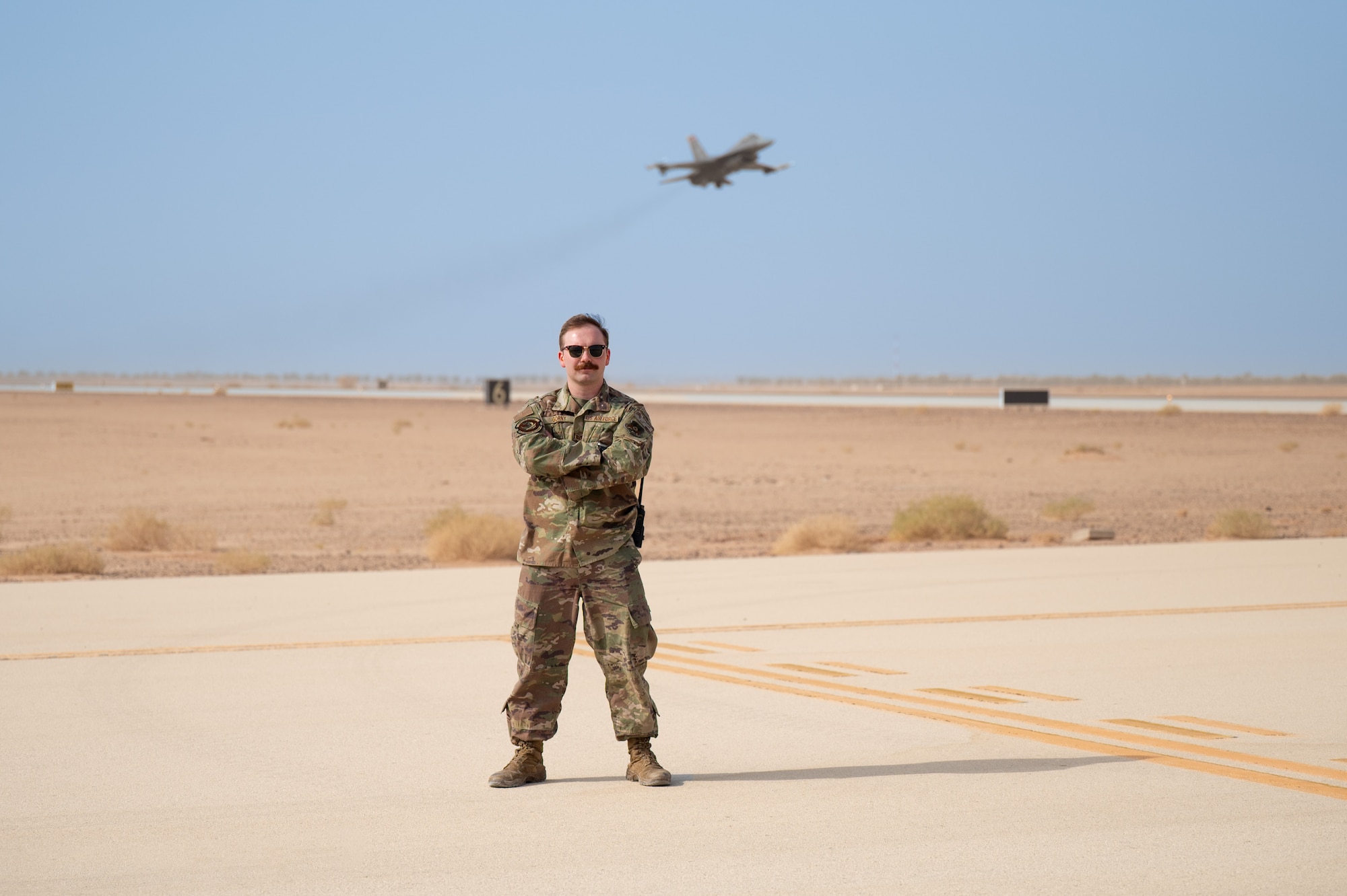 Airman poses on the flightline as an F-16C takes off behind him