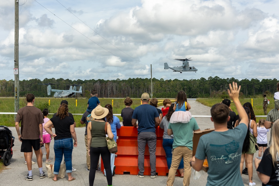 U.S. service members and their families watch an MV-22 Osprey tiltrotor aircraft demonstration during a family day event at Camp Davis, Marine Corps Base Camp Lejeune, North Carolina, Aug. 23, 2025. The 26th Marine Expeditionary Unit hosted a family day for the Special Purpose Marine Air-Ground Task Force – Alert Contingency MAGTF (SPMAGTF-ACM) to give Marines and Sailors a chance to show their family members a glimpse of their day-to-day duties while also offering hands-on demonstrations of Marine Corps equipment and weapons. (U.S. Marine Corps photo by Lance Cpl. Jack Labrador)