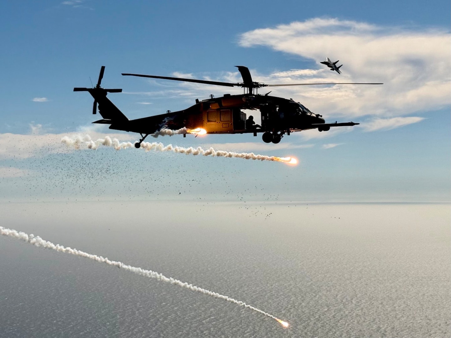 U.S. Air Force HH-60G Pave Hawk helicopter assigned to the 129th Rescue Squadron, California Air National Guard deploys countermeasure flares as a U.S. Air Force F-15D Eagle from the 144th Fighter Wing, California Air National Guard, maneuvers overhead during a joint over-water test flight, Aug. 20, 2025.