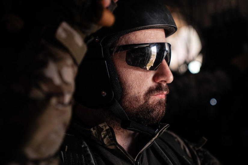 A bearded man wearing a helmet and sunglasses looks to the right.