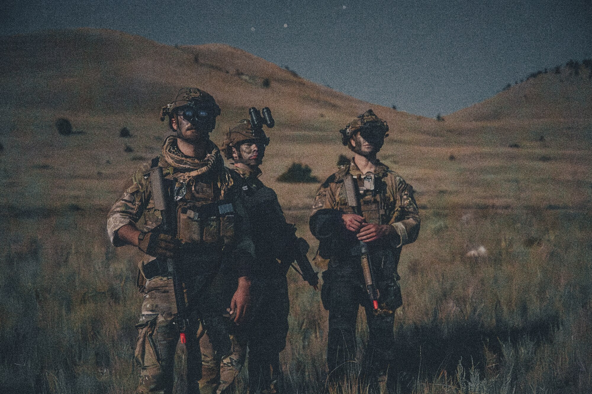 Three Airmen standing in a field covered in full combat gear.