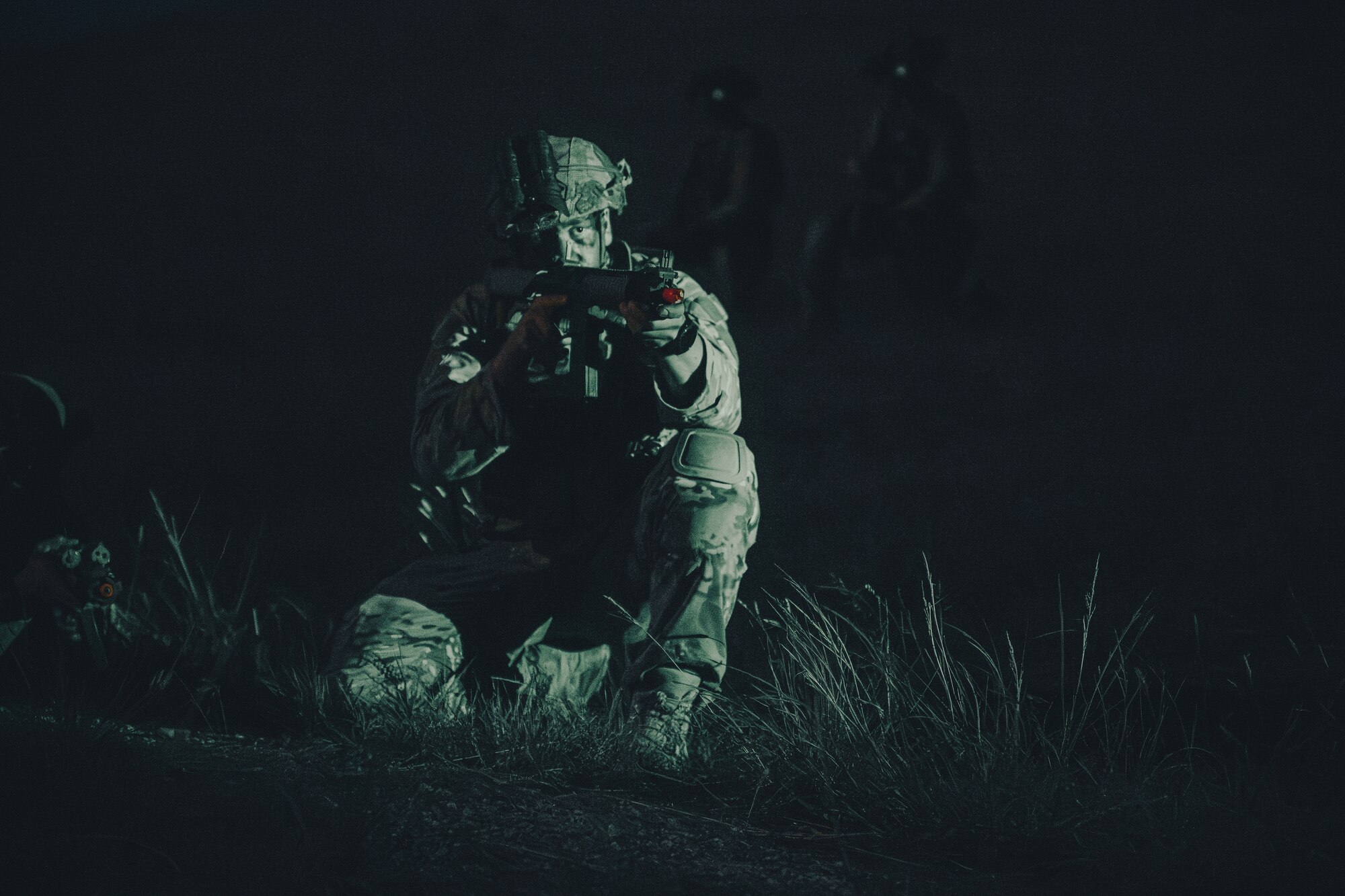 A night photo with an Airman on his knees with a light shining on him.