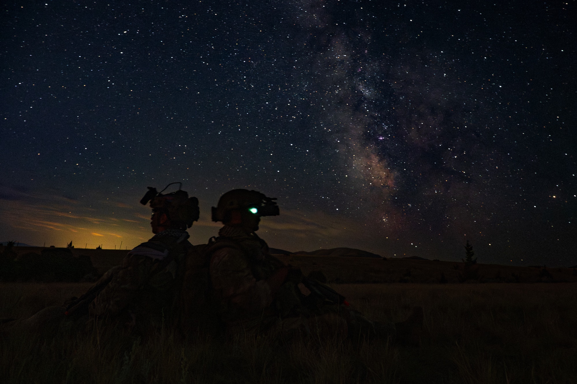 A silhouette of two Airmen sitting back to back with stars in the background
