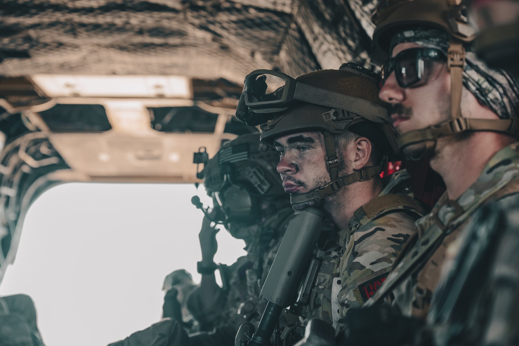 Airmen sit in the interior of a helicopter.